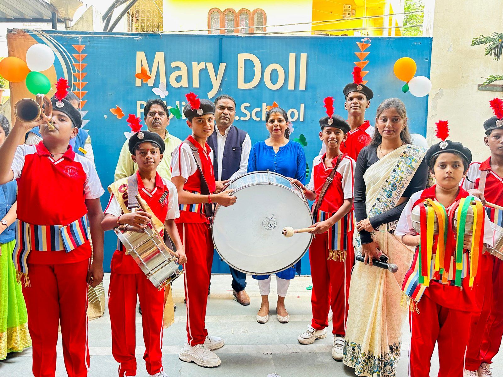 The MDPS school band and house captains in red uniforms, drums and sashes, in front of the school banner