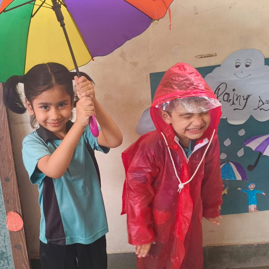 Two little ones on Rainy Day, one under a striped umbrella and one in a red raincoat